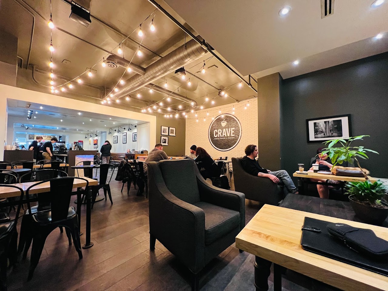 Inside CRAVE: warm wood tables, glowing pendant lights and the café’s logo on a cream brick wall